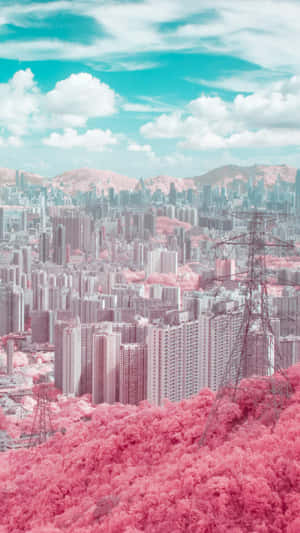 在藍綠色天空下，粉紅色森林覆蓋的山丘聳立在現代城市旁邊。