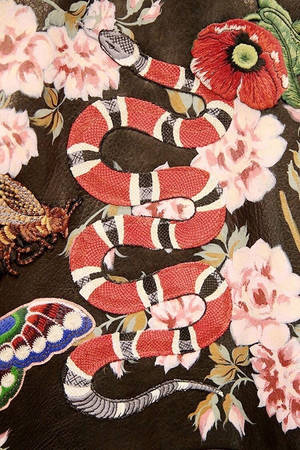 深色布料上被花朵和昆蟲包圍的刺繡蛇。