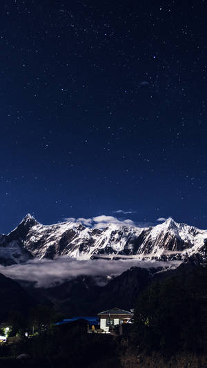 星空夜幕下的積雪山峰，山谷中亮燈的房子。