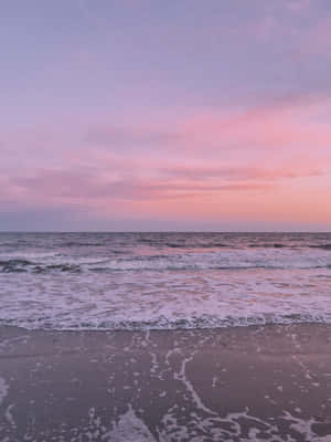 粉紅色和紫色的日落映照在濕沙上的海浪