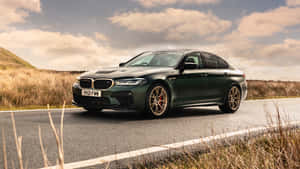 啞光綠色BMW M5在鄉村道路上行駛，兩旁有金色草和陰天。