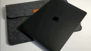 黑色MacBook放在灰色氈套上，帶橙色細節，置於白色表面