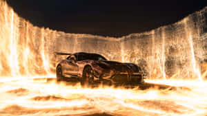 夜晚，黑色跑車被火焰和火焰瀑布包圍。 — Studio Display 壁紙