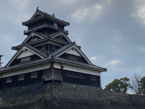 傳統日本城堡塔樓，層疊屋頂和石質底座，在多雲的天空下。
