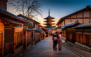 兩位身穿和服的女士在日落時分沿著傳統日本小巷走向寶塔。