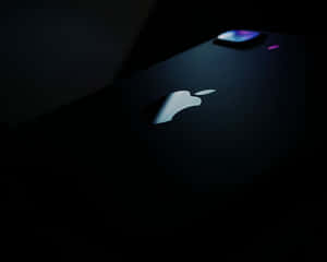 在昏暗光線下，帶有發光Apple標誌的黑色iPhone特寫。