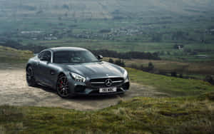 日落時分，灰色 Mercedes-AMG GT 停在青草山坡上，俯瞰鄉村山谷。