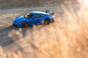 藍色保時捷911 GT3 RS在日落時分的碎石路上揚起塵土漂移。