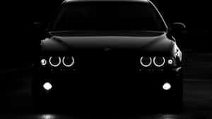 黑色BMW汽車在黑暗中亮著車頭燈的前視圖。