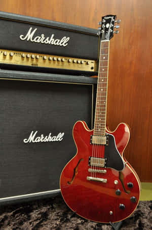 紅色電結他企喺兩部Marshall擴音機旁邊，背景係木牆。