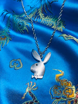 銀色Playboy兔仔吊墜項鍊在藍色刺繡緞布上。