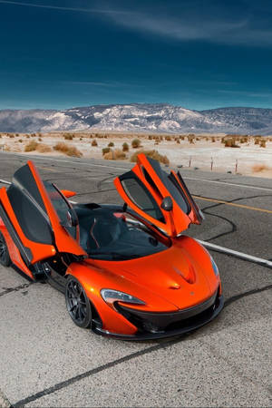 橙色McLaren跑車，車門打開，在沙漠公路上，靠近山脈，日落時分。
