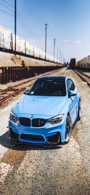 藍色BMW M4在日落時停泊在鐵路軌道旁的礫石上。 — Galaxy A16 壁紙