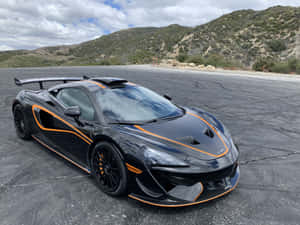 黑色McLaren跑車帶橙色飾邊停在瀝青地上，靠近山丘。
