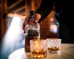 在燈光昏暗的酒吧裡，手拿著威士忌瓶和兩個杯子放在木桌上。