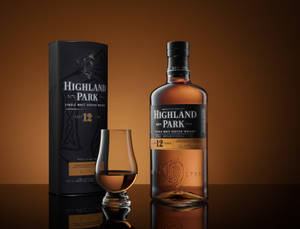 Highland Park 12 年威士忌瓶，附玻璃杯和盒子，置於反射表面。