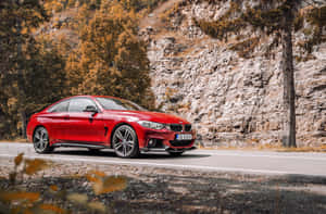 紅色BMW雙門跑車在秋葉和岩石峭壁的山路上行駛。