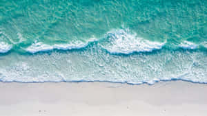 碧綠色的海浪輕輕湧上白色沙灘的俯瞰圖。