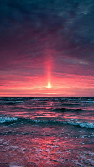 海洋上空鮮豔的日落，紅色和紫色的天空倒映在水面上。