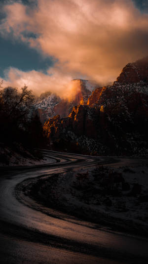 日落時分，金色光芒穿透雲層，照耀著蜿蜒的雪路穿過群山。
