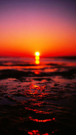 海洋上的夕陽，鮮豔的橙色和紫色天空反射在濕沙上。