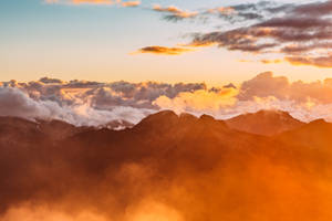 夕陽映照霧氣繚繞的山巒，雲彩發出橙色光芒