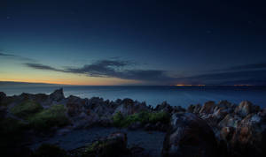 夜晚的岩石海岸，星空下遠方的城市燈光。