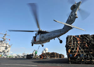 海軍直升機在航空母艦甲板上吊起貨物，船員在附近。 — 直升機 壁紙