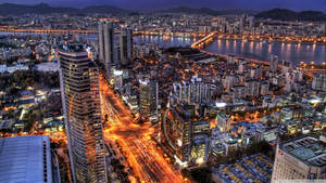 充滿活力的城市夜景鳥瞰圖，建築物閃爍，河畔橋樑明亮。 — 韓國 壁紙