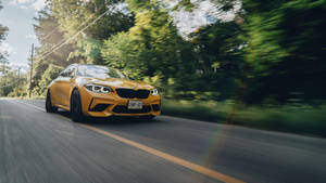 黃色BMW M2在陽光明媚的森林道路上疾馳，帶有動態模糊效果。