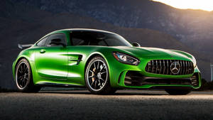 綠色 Mercedes-AMG GT 跑車停在日落時分有山脈的道路上。