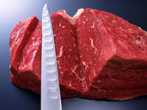 在深色表面上用鋸齒刀切開的生牛肉。