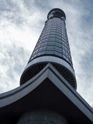 從下方仰望高聳的現代摩天大樓，背景是多雲的天空。 — 日產 Skyline GTR R33 壁紙