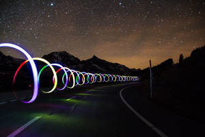 色彩繽紛的光圈沿著山路在繁星點點的夜空下延伸。 — 夜空 壁紙