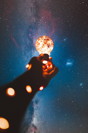 手在銀河下的星空夜空中拿著發光的燈泡