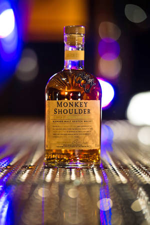 Monkey Shoulder威士忌酒瓶放在吧枱上，伴隨色彩繽紛的燈光和倒影。 — 小米Pad 7 Ultra 壁紙