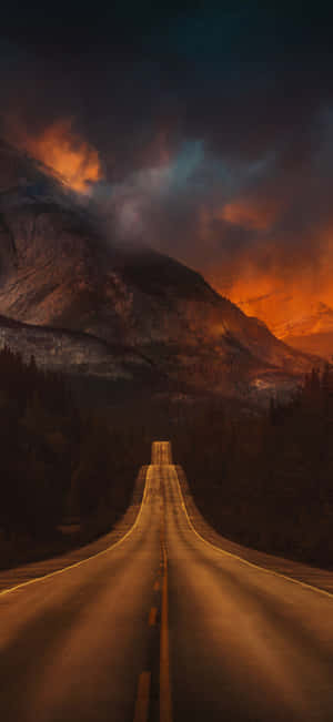 一條蜿蜒穿過森林的道路在戲劇性的暮色天空下通往群山。