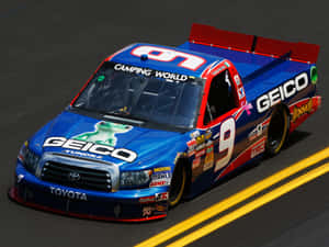 帶有 GEICO 標誌的藍色和紅色 NASCAR 賽車卡車在賽道上飛馳。