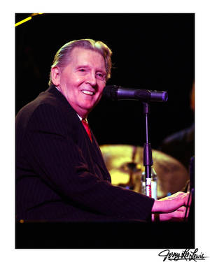 Jerry Lee Lewis 在舞台上微笑彈奏鋼琴，旁邊有麥克風。