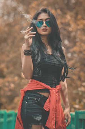 一位戴太陽眼鏡和紅色外套的女性在戶外秋天抽煙。