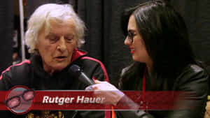 Rutger Hauer 正接受一位戴眼鏡、手持咪高峰的女子訪問。