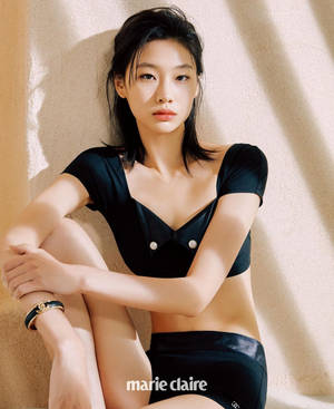 一位身穿黑色緞面內衣的女性在陽光照射、帶有紋理的牆前擺姿勢。
