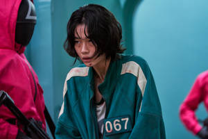 一名身穿青綠色魷魚遊戲制服、編號067的參賽者看起來緊張又害怕。