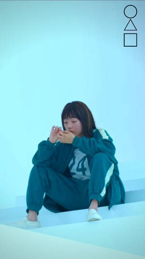 年輕女性身穿青綠色運動服，坐在極簡風格工作室的白色台階上，周圍有幾何形狀。