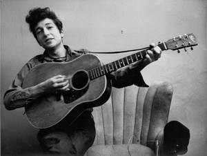 Bob Dylan 在一張黑白工作室肖像照中手持木結他。