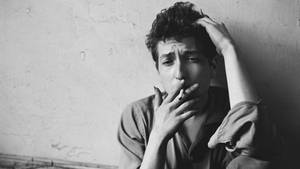 一個捲髮男人靠牆抽煙的黑白肖像。
