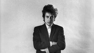 Bob Dylan 穿著黑色西裝交叉雙臂嘅工作室肖像。