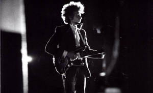 Bob Dylan 在黑白照片中於舞台上彈奏電結他。