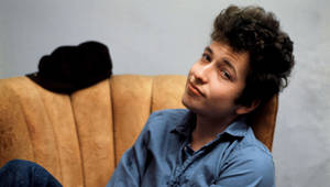 年輕的Bob Dylan坐在米色梳化上，身穿藍色襯衫和牛仔褲，身後有一頂黑色帽子。