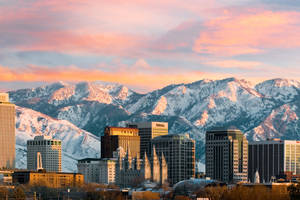 粉紅日落天空下，城市天際線與白雪覆蓋的山峰。